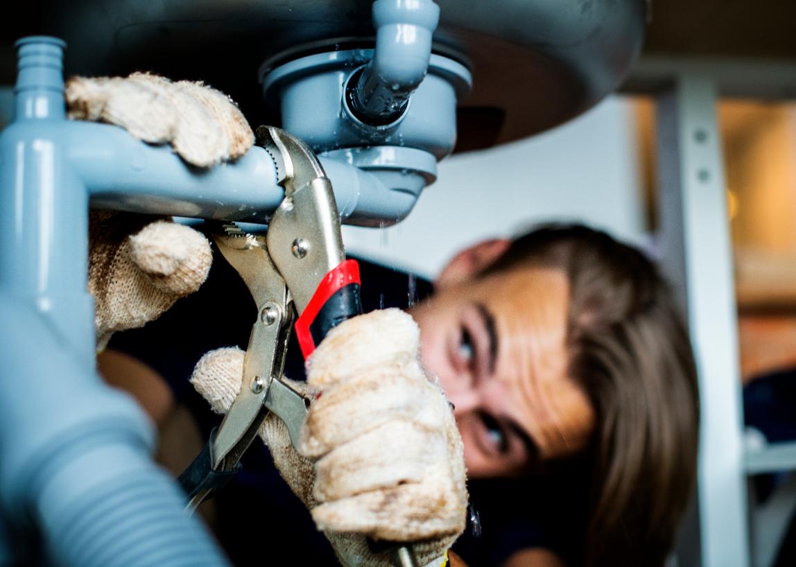 Plumber repairing pipework beneath a kitchen sink